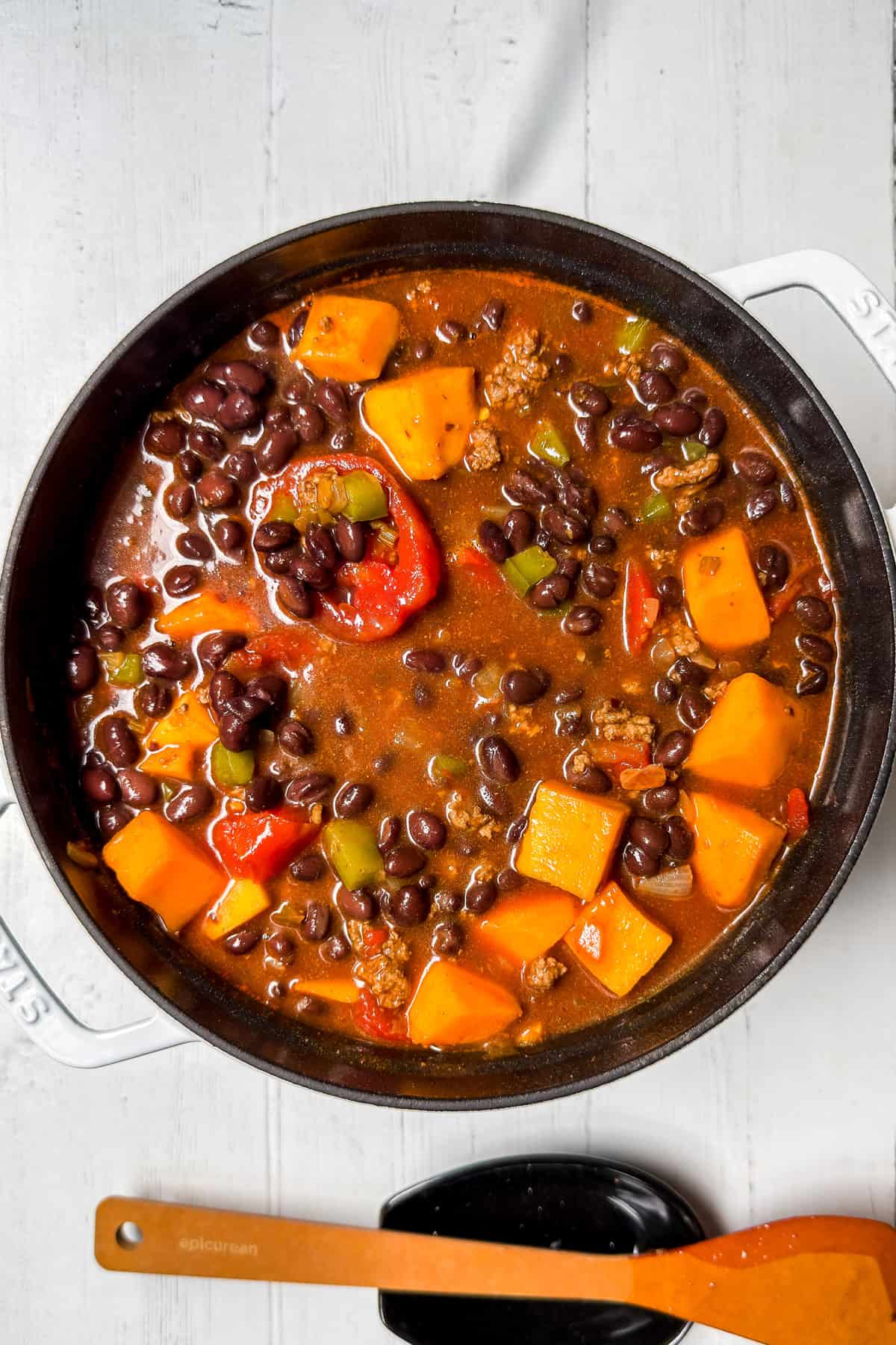 Adding butternut squash and black beans to the chili in a large pot.