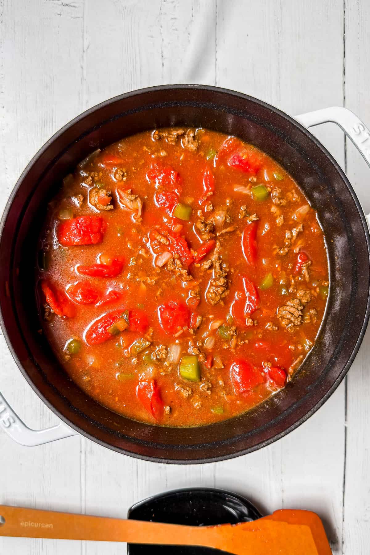 Broth and tomatoes added to the beef and butternut squash chili base in a large pot.