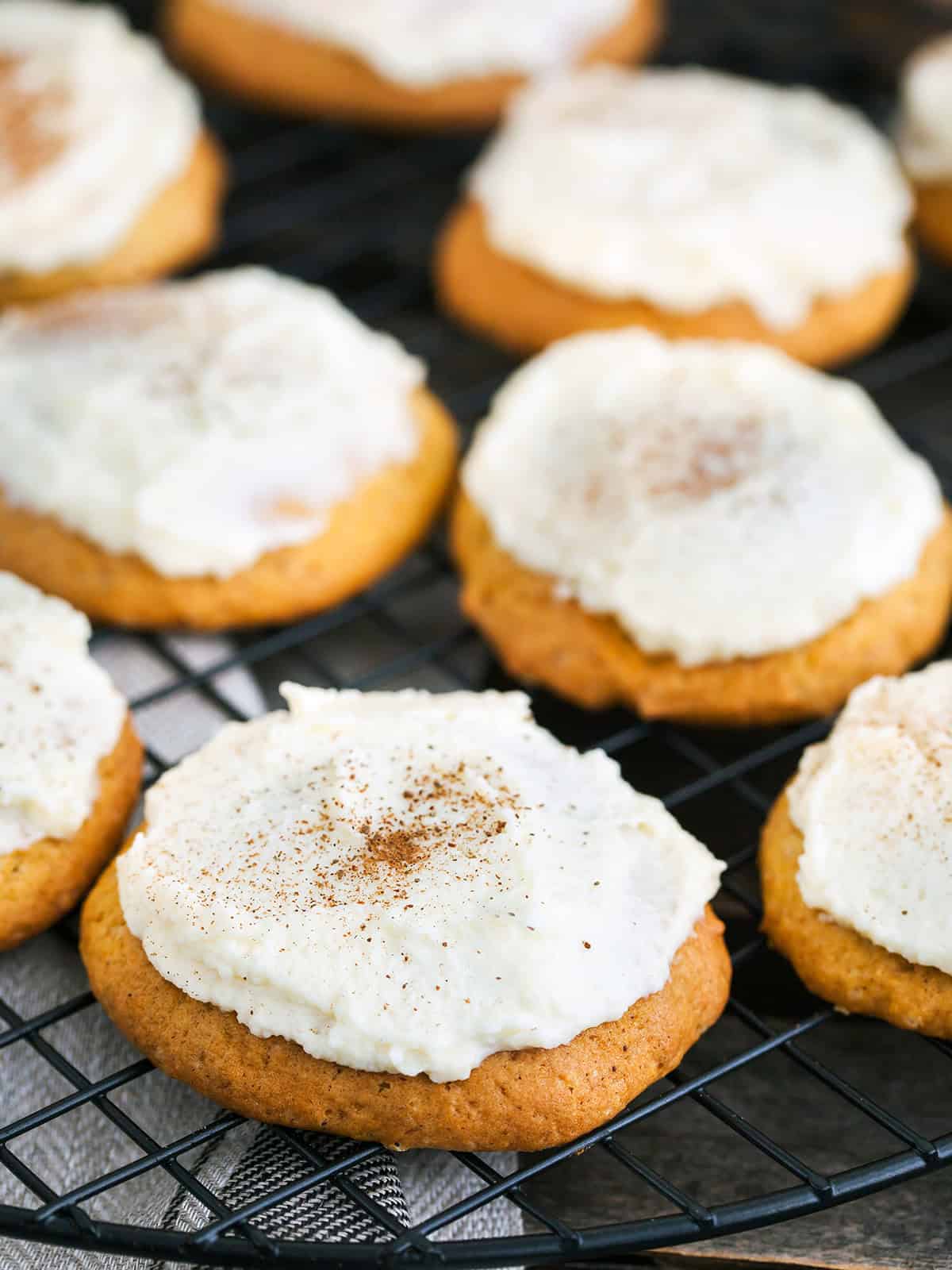 Closeup of a soft pumpkin spice cookie topped with vanilla frosting and a dusting of spice.
