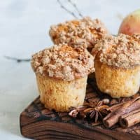 Muffins on a wooden board with apples and cinnamon sticks.