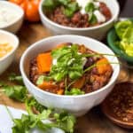 Bowl of Beef and Butternut Squash Chili, garnished with fresh cilantro, in a bowl with shredded cheese and sour cream on the side.