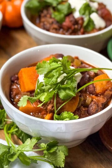 Bowl of Beef and Butternut Squash Chili, garnished with fresh cilantro, in a bowl with shredded cheese and sour cream on the side.