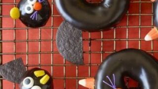 Chocolate-glazed donuts and donut holes decorated with candy and cookies to resemble bats and cats make delightful Spooky Halloween Treats, arranged perfectly on a wire cooling rack.