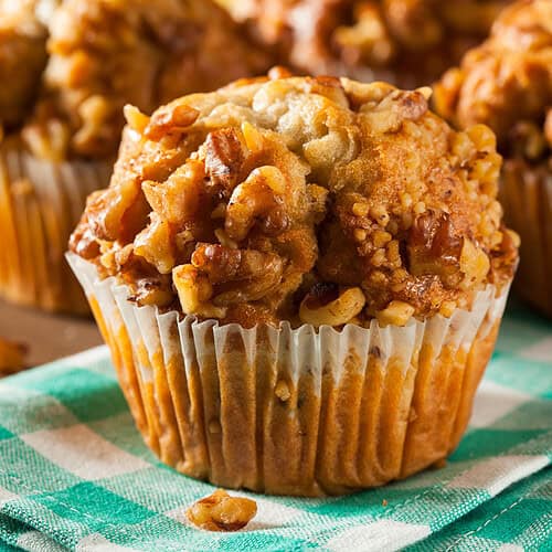 Closeup horizontal image of Banana Ginger Muffins resting on a green and white check linen with more in the background.