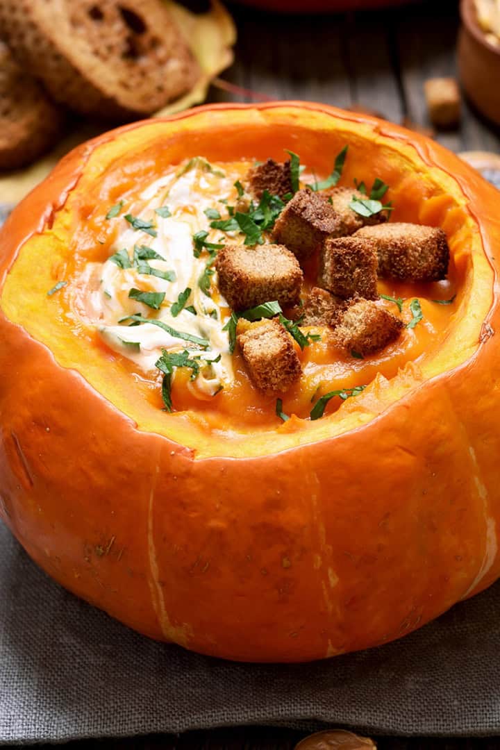 Square closeup image of pumpkin curry soup in a hollow roasted sugar pumpkin on a wooden serving board.