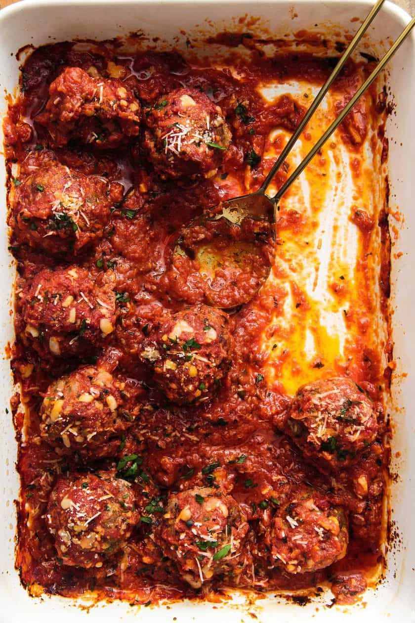 Baking dish with meatballs in tomato sauce, partially served, with a serving spoon and sauce remnants on the side-perfect as Easy New Year's Eve Appetizers for your festive gathering.