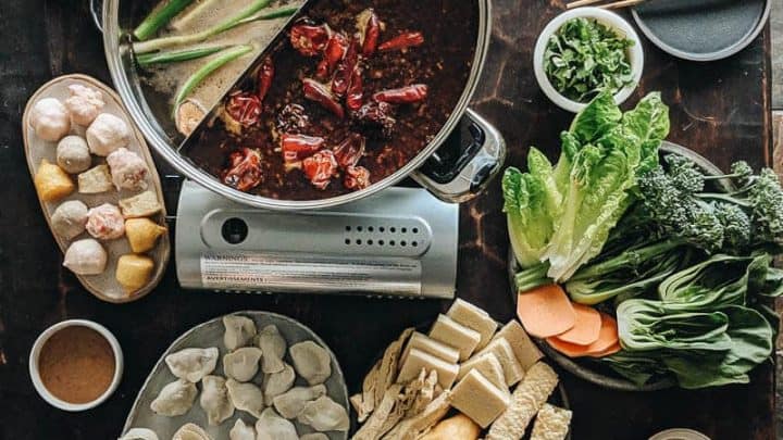 A table set for Lunar Chinese New Year with a divided hot pot, sliced meats, various vegetables, noodles, tofu, dipping sauces, and other festive hot pot ingredients arranged around the pot.