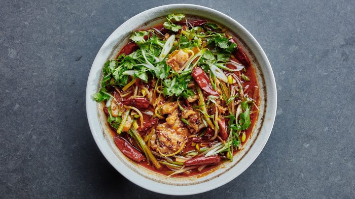 A bowl of spicy noodle soup with pieces of chicken, dried red chilies, green onions, and fresh cilantro on a dark surface—perfect for celebrating Lunar Chinese New Year.