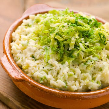 Colcannon-style mashed potatoes topped with shredded green cabbage, served in a rustic brown ceramic dish.