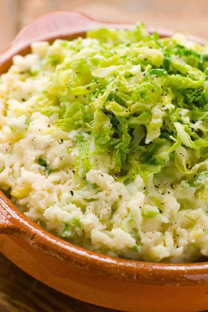 Colcannon-style mashed potatoes topped with shredded green cabbage, served in a rustic brown ceramic dish.