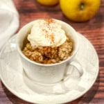 Baked Apple Crisp topped with vanilla ice cream and cinnamon in a white mug.