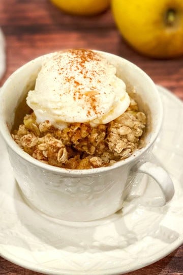 Baked Apple Crisp topped with vanilla ice cream and cinnamon in a white mug.