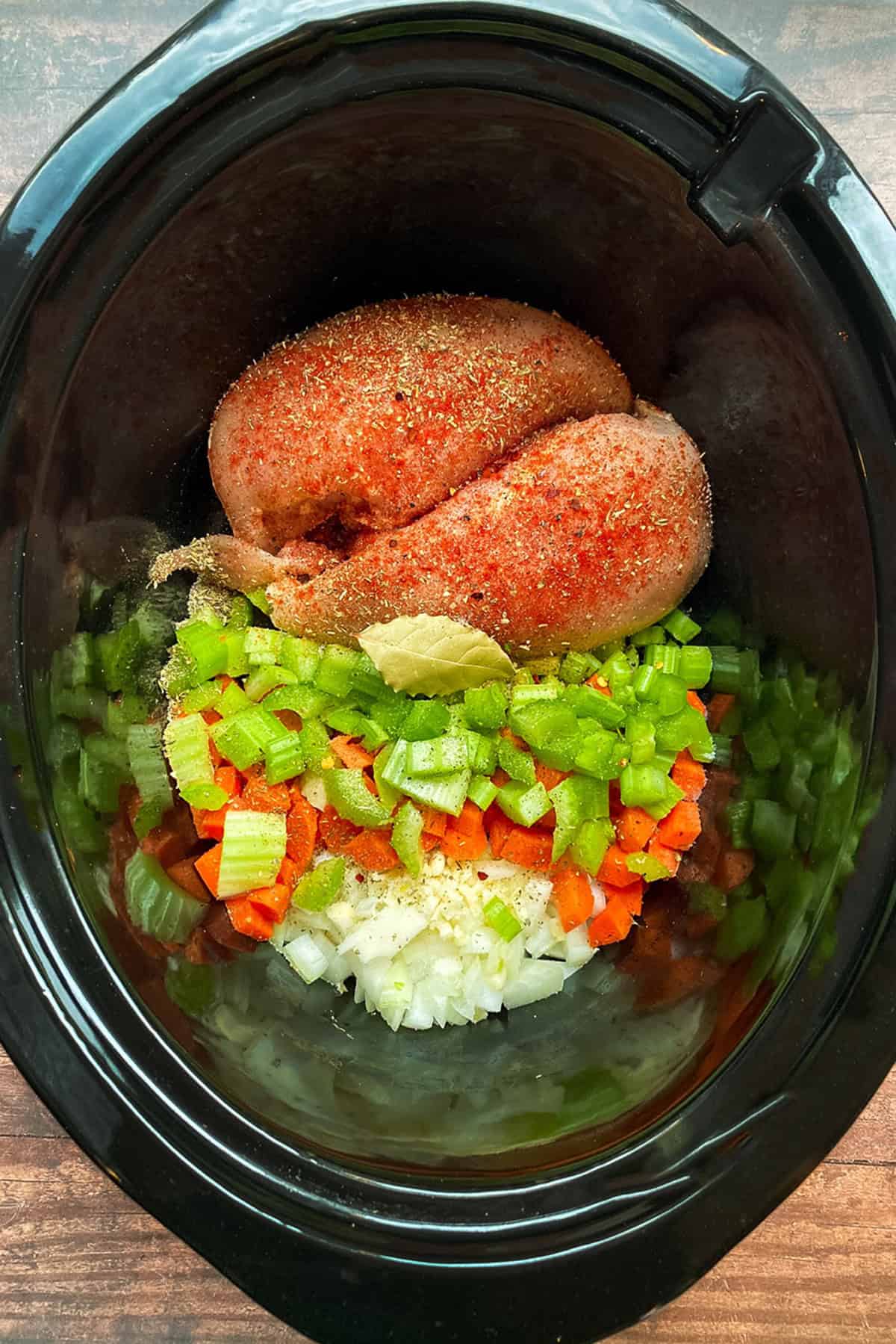 Raw chicken noodle soup ingredients, seasoned and ready for broth in a slow cooker insert.