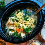 Chicken Noodle Soup with egg noodles and greens in a black slow cooker insert ready for serving.