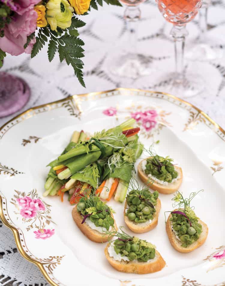 An ornate floral plate with five crostini topped with mashed peas and microgreens, served beside a small pile of mixed vegetable salad-perfect for a charming spring afternoon tea.