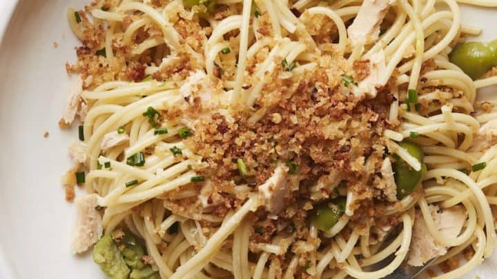 A plate of spaghetti with green olives, chunks of tuna, herbs, and toasted breadcrumbs—one of those pantry staple recipes—served with a fork.