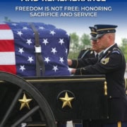 Two uniformed soldiers stand by a flag-draped casket on a carriage, honoring Memorial Day and the sacrifices of military service members.