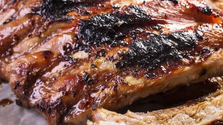 Grilled Baby Back Ribs with a glossy glaze and char marks, served on parchment paper and garnished with a fresh sprig of rosemary.