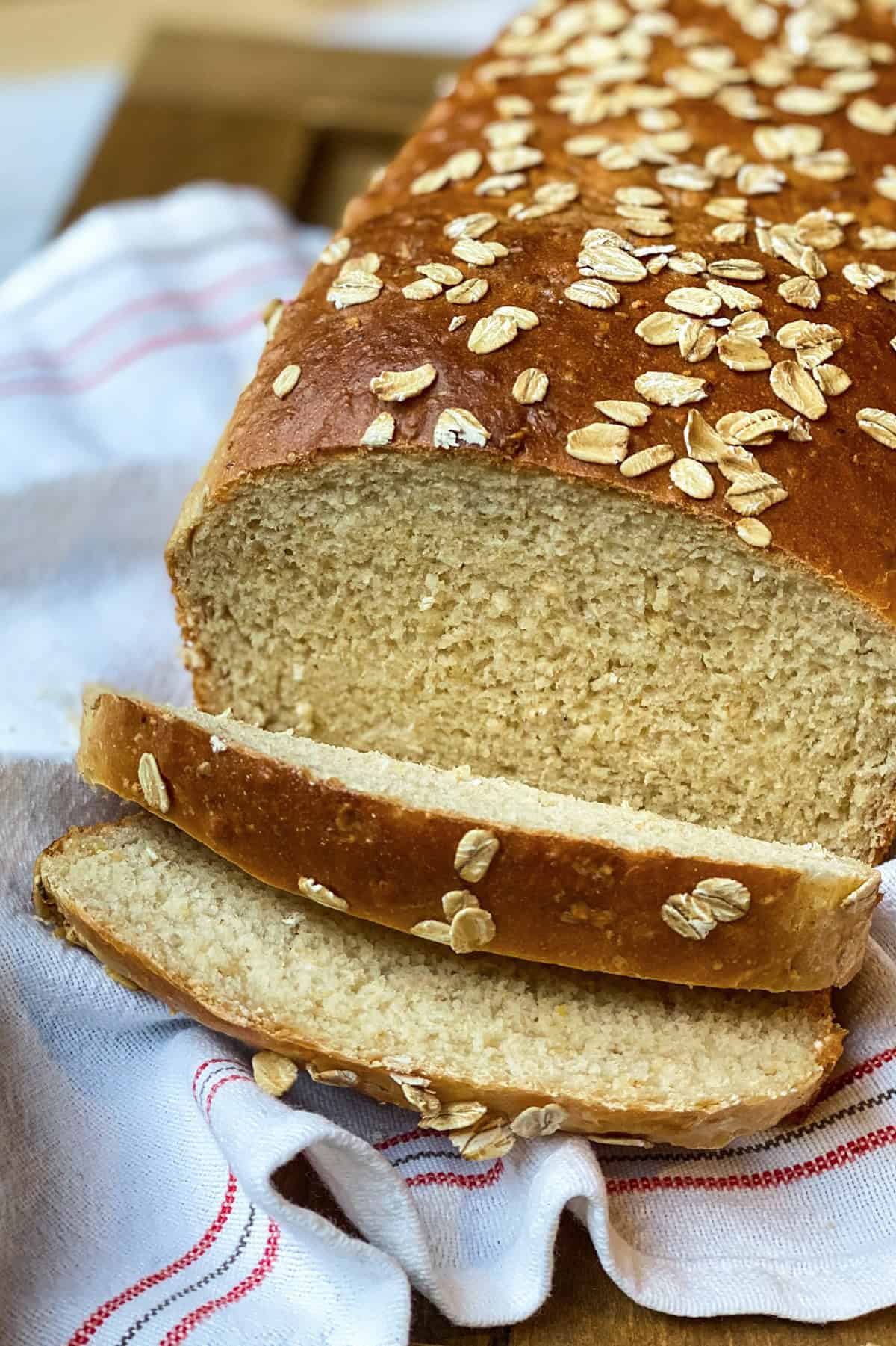 Sliced honey oat sandwich bread topped with oats on a linen lined wooden tray.