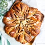 Golden-brown star-shaped babka bread with twisted segments, drizzled with white icing, on parchment paper atop a wooden board.