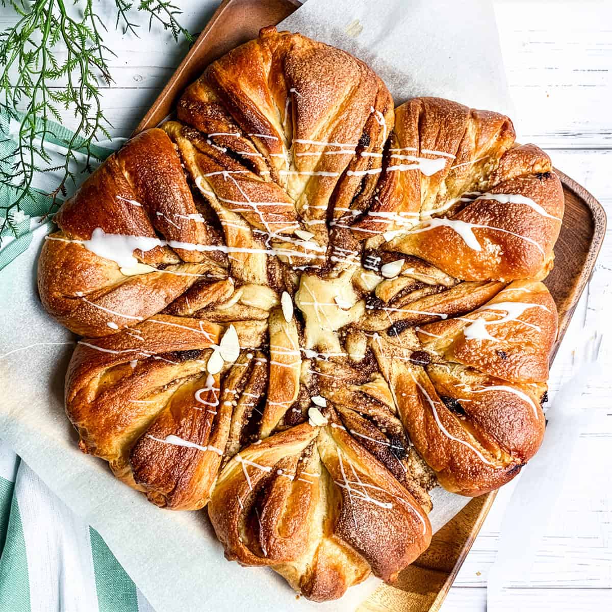 Golden-brown star-shaped babka bread with twisted segments, drizzled with white icing, on parchment paper atop a wooden board.