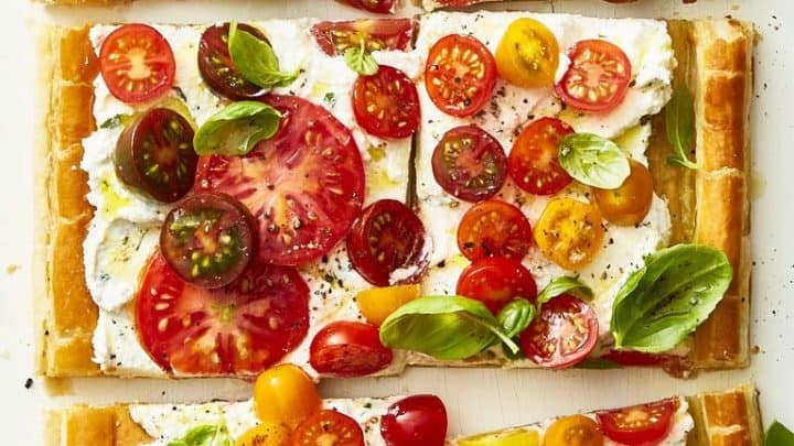 Rectangular puff pastry tart cut into six pieces, topped with whipped cheese, colorful tomatoes, black pepper, and fresh basil—perfect for adding to your list of easy Mother's Day recipes.