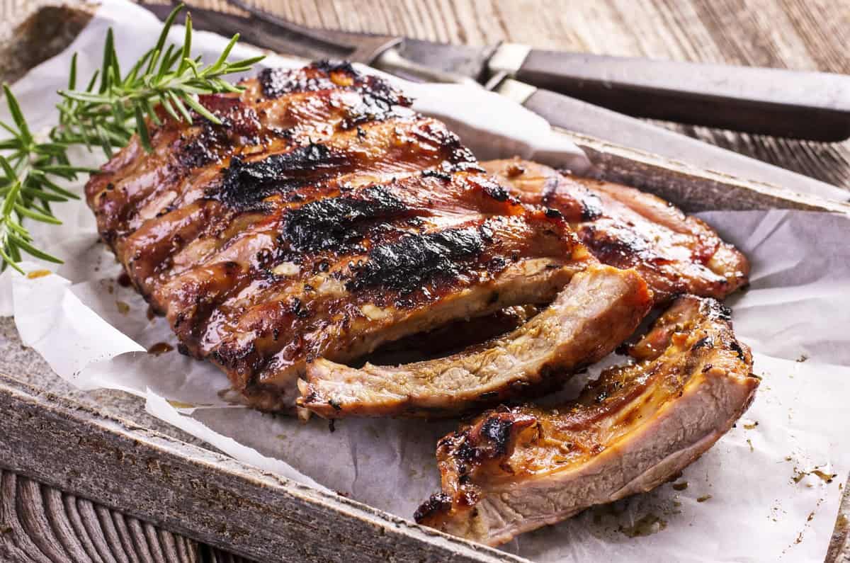 Perfectly grilled baby back ribs, cut into portions with a sprig of fresh rosemary on a wooden serving board.