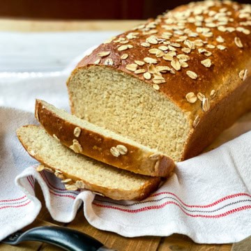 Sliced Honey Oat Bread loaf on a linen lined wooden tray ready for sandwich making.
