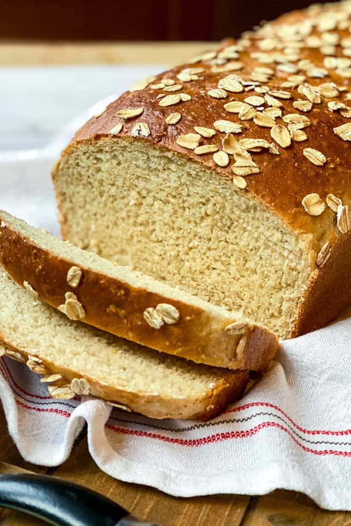 Sliced Honey Oat Bread loaf on a linen lined wooden tray ready for sandwich making.