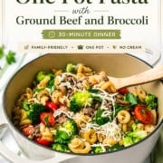 A pot of One Pot Pasta with ground beef, broccoli, tomatoes, mushrooms, and cheese sits on a kitchen counter with a wooden spoon, garnished with herbs. Text overlay promotes this easy and delicious dish.