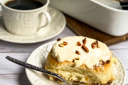 Homemade Cinnamon Roll on a White Plate with a Cup of Coffee