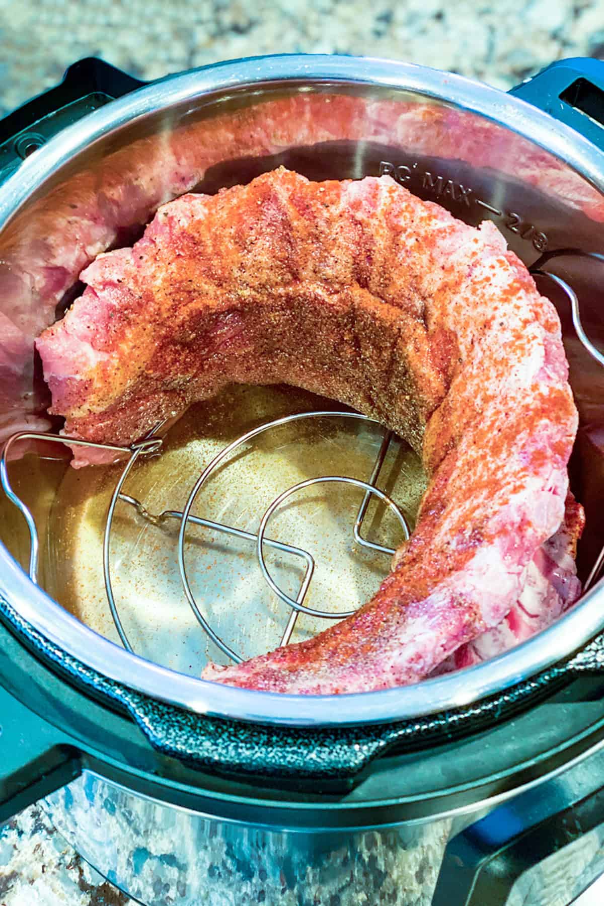 Raw, seasoned pork ribs arranged in a ring on a metal rack inside an Instant Pot, these Easy Instant Pot Ribs are ready for pressure cooking.