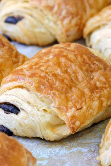 Easy chocolate croissants with flaky puff pastry on parchment lined baking dish.