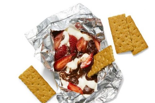 Foil packet featuring melted chocolate, marshmallows, and strawberries, surrounded by four pieces of graham crackers on a white background-perfect for Memorial Day Desserts.