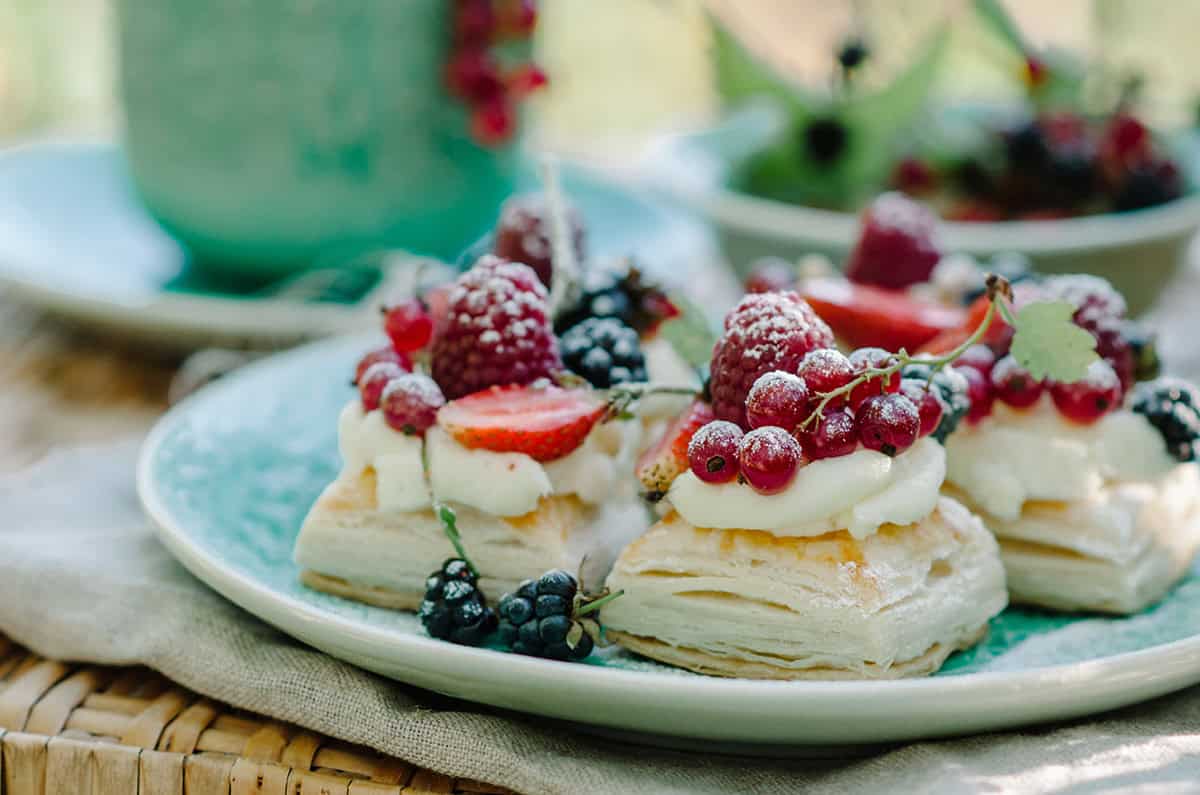 Three puff pastry tarts topped with lemon cream and assorted berries are served on a light blue plate.
