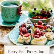 A plate of delicate puff pastry tarts with lemon cream, topped with assorted fresh berries, sits beside a cup of tea on a wicker surface.