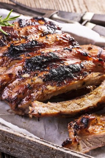 A rack of grilled barbecue ribs with a slightly charred surface, perfect for a 4th of July Cookout, garnished with rosemary and served on parchment paper in a rustic wooden tray.