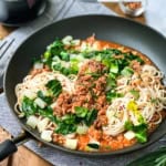 A bowl of pasta with cream sauce, mushrooms, and chopped green onions, reminiscent of the comforting flavors found in ginger pork noodles, with a fork resting on the side of the bowl.