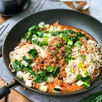 A bowl of pasta with cream sauce, mushrooms, and chopped green onions, reminiscent of the comforting flavors found in ginger pork noodles, with a fork resting on the side of the bowl.