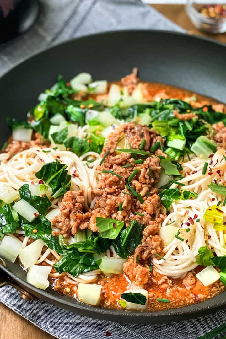 A bowl of pasta with cream sauce, mushrooms, and chopped green onions, reminiscent of the comforting flavors found in ginger pork noodles, with a fork resting on the side of the bowl.