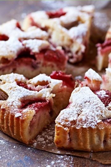 Sliced strawberry rhubarb cake topped with powdered sugar, displayed on parchment paper.