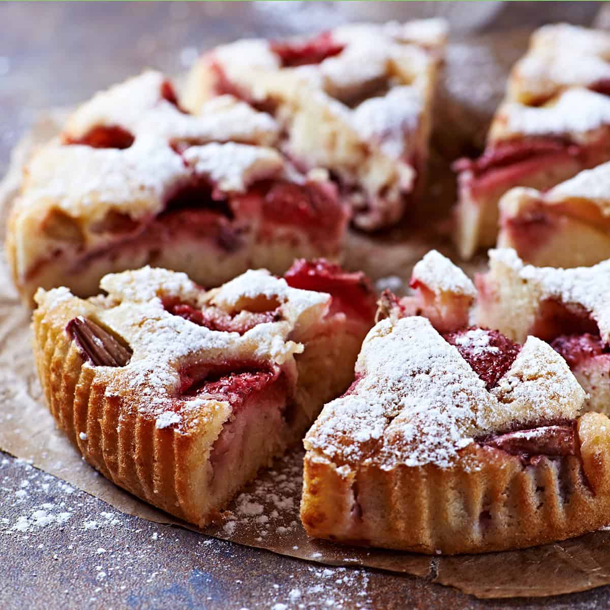 Sliced strawberry rhubarb cake topped with powdered sugar, displayed on parchment paper.