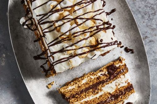 A rectangular layered dessert with cream, chocolate drizzle, and marshmallows is displayed on an oval metal tray, with one slice cut and placed beside it-perfect for Father's Day Dessert Recipes.