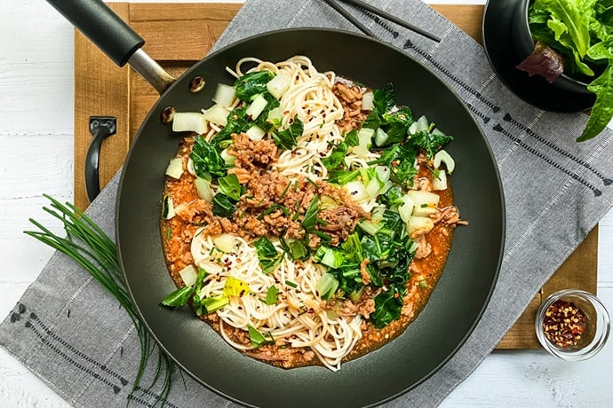 Closeup of Ginger Pork Noodles with Bok Choy in a Black Skillet
