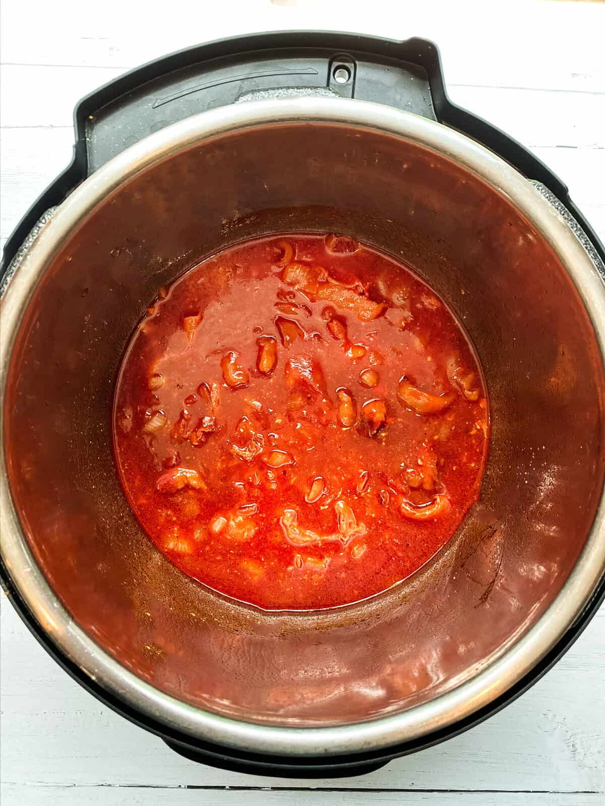 A stainless steel pot filled with chunky tomato sauce sits on a white surface, viewed from above. The sauce contains visible tomato pieces and resembles the hearty texture of Instant Pot Baked Beans, cooked inside an electric pressure cooker.