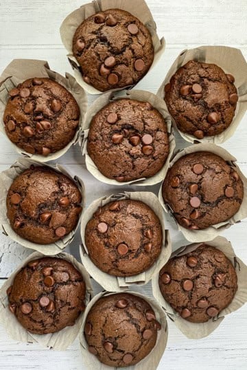 Chocolate Zucchini Muffins in paper sleeves resting on a wooden serving board.