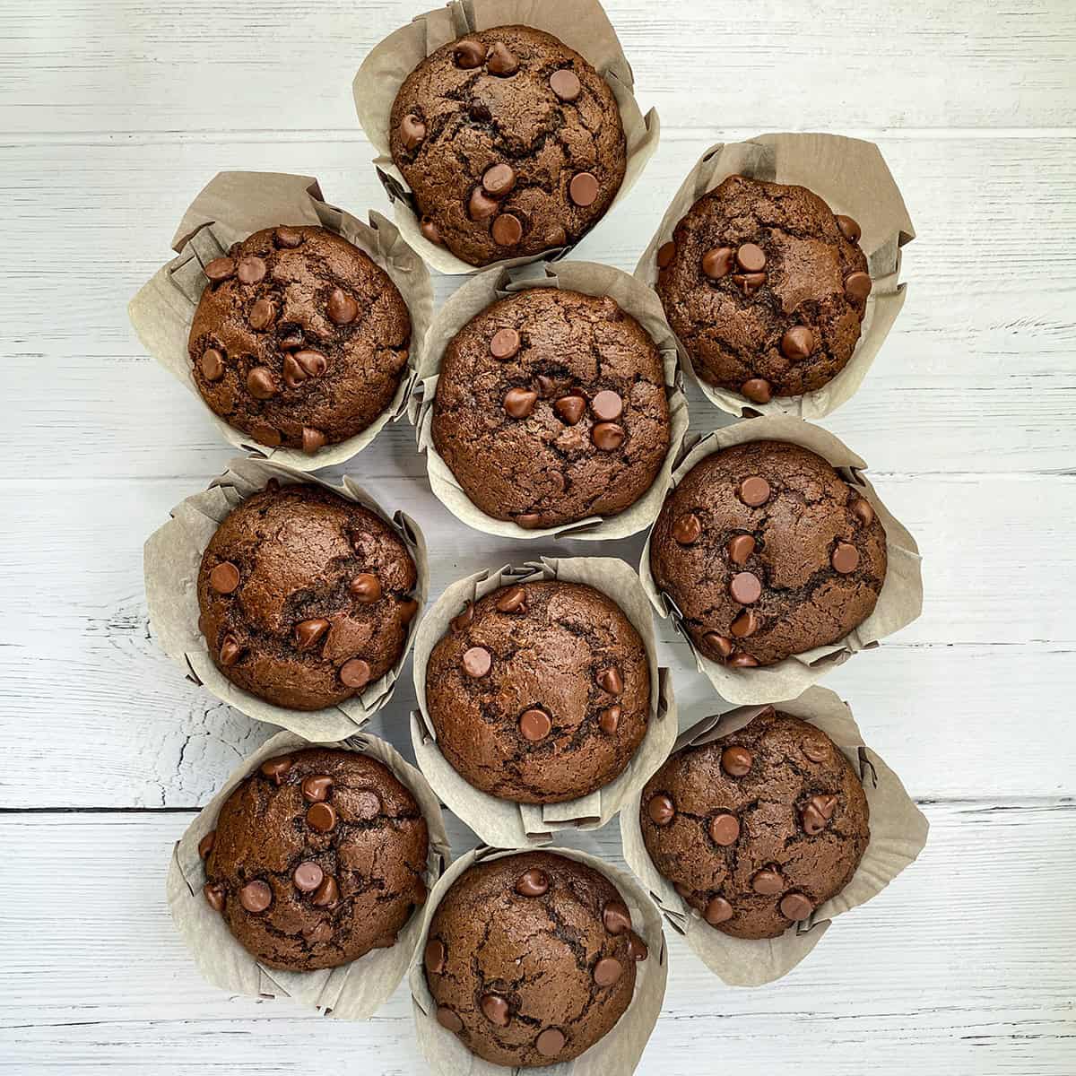 Chocolate Zucchini Muffins in paper sleeves resting on a wooden serving board.