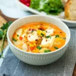 Bowl of fish chowder garnished with fresh herbs resting on a wooden serving tray.