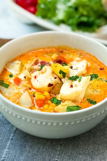 Bowl of fish chowder garnished with fresh herbs resting on a wooden serving tray.