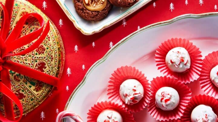 Five decorated Vintage Christmas Cookies with white icing and red candy are arranged on a wooden surface with a red cloth and green holly-shaped sprinkles.